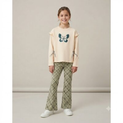 Smiling girl wearing a beige sweater with a blue butterfly graphic, plaid green pants, and white sneakers in a studio setting.