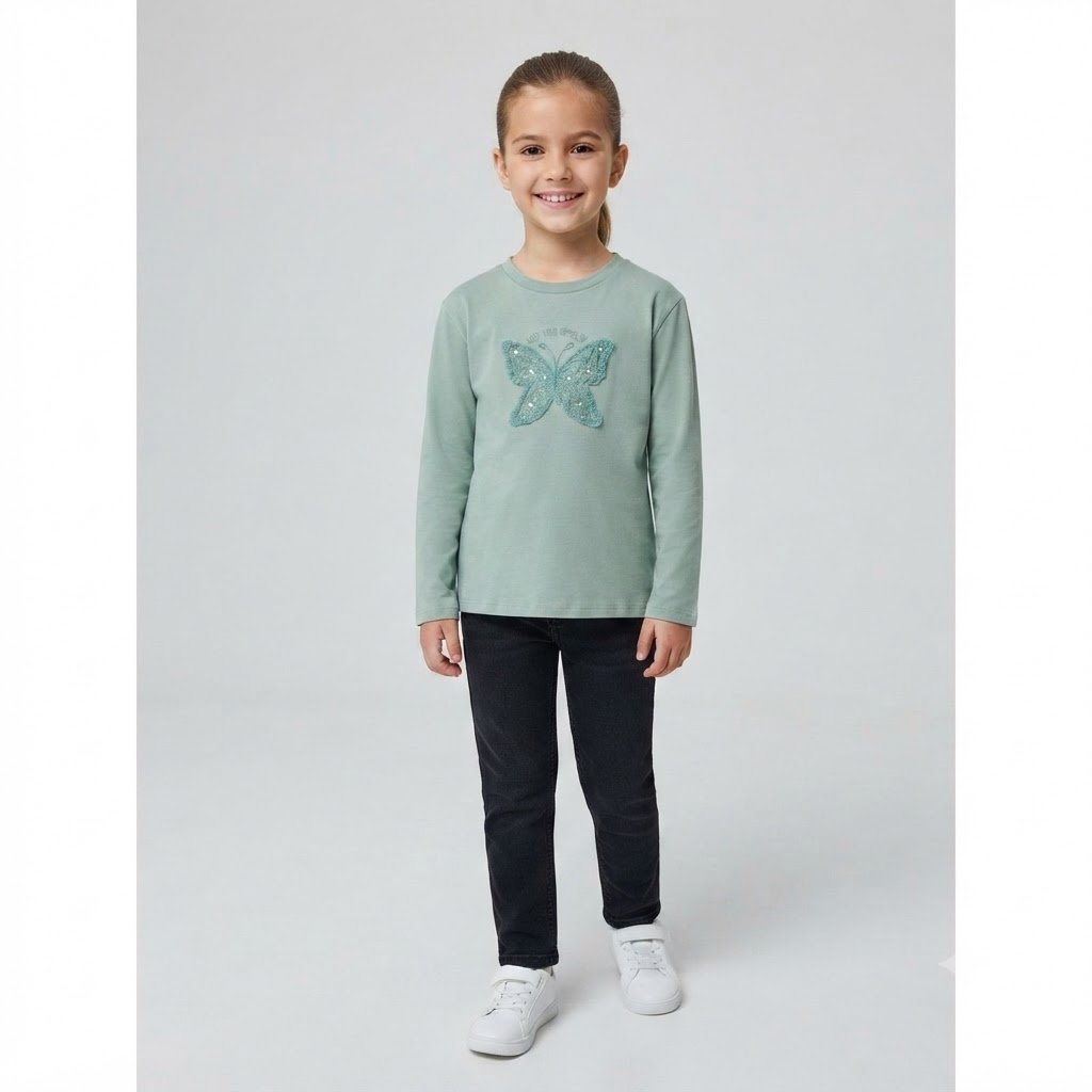 e34779c1-08b7-4778-9082-0fd297501875 - Da-Da Kids Smiling girl in a mint-green long-sleeve shirt with a glitter butterfly graphic, dark jeans, and white sneakers, standing in a neutral studio.
