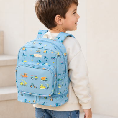 Young boy in a beige sweater wearing a blue backpack with construction vehicle pattern, standing on steps.