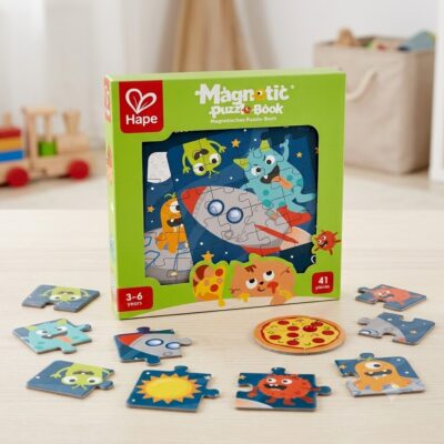 Green Hape Magnetic Puzzle Book box on a light floor, with scattered colorful puzzle pieces around a circular pizza tile nearby.